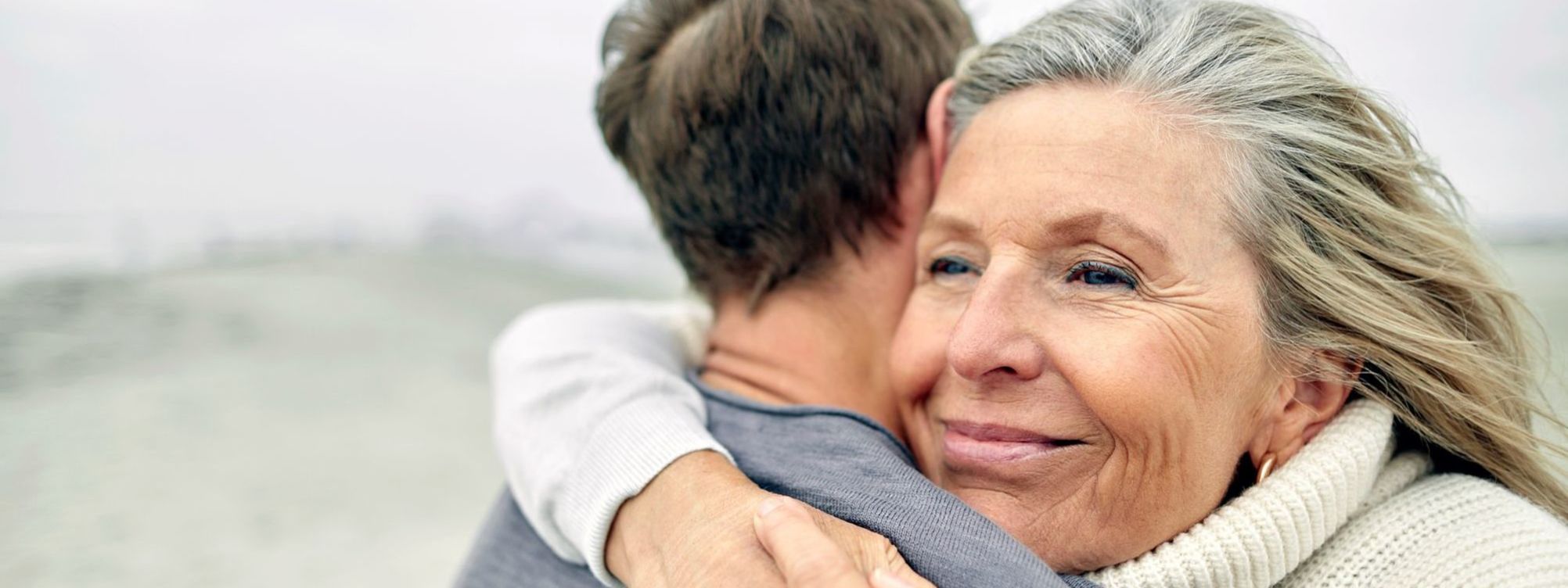 Harrington Discovery Institute Accelerates Breakthrough Science into Cancer Treatments and Cures. Harrington Advances Science to Medicine through Philanthropy. The image portrays a middle-aged woman hugging a male family member on a beach. .